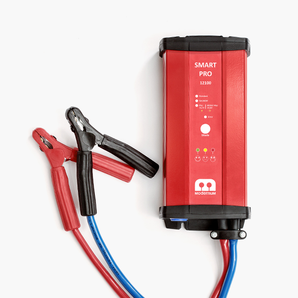 Modernums batteriladdare (röd) med två kablar som leder till batteriklämmor.